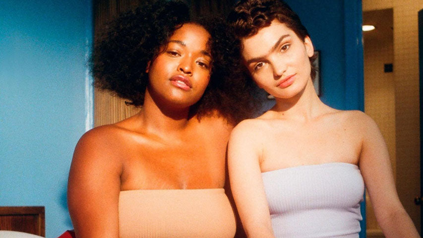 Partners wearing strapless tops looking into the camera while a glowing light illuminates them for a portrait.