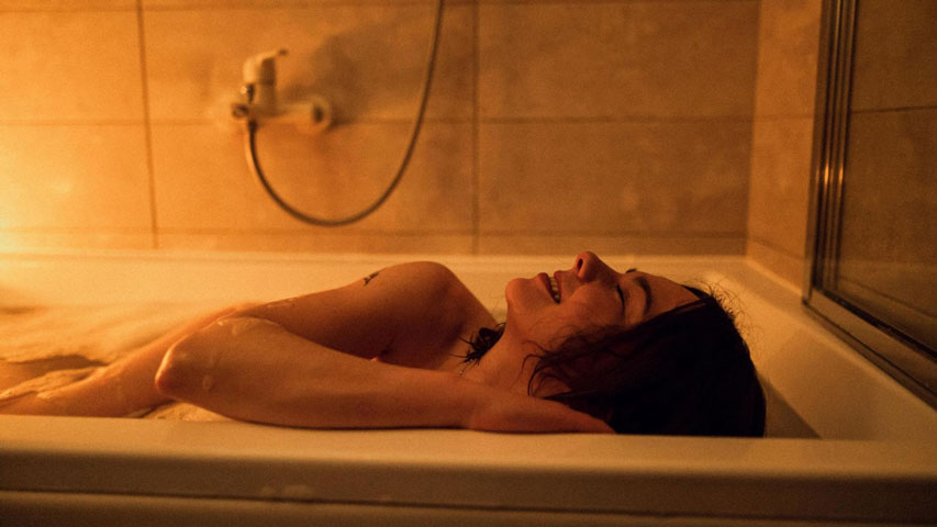 Une femme sourit dans un bain, sachant exactement comment bien utiliser son jouet sexuel sous l’eau.