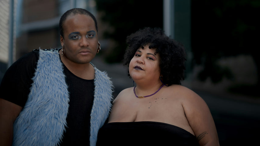 Two friends gaze fiercely into the camera while wearing vibrant makeup.