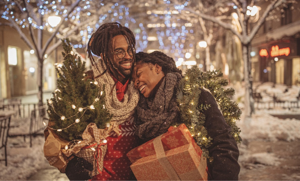 Couple leans into each other lovingly with holiday supplies in hand.