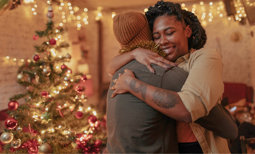 Two partners hug in front of an indoor light display and Christmas tree.