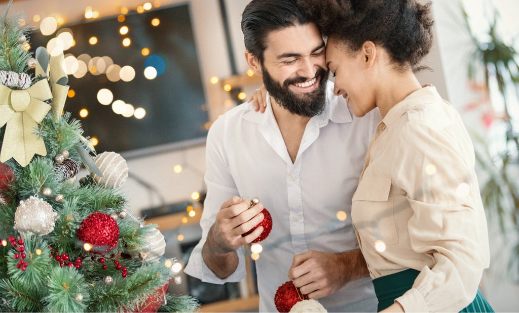 Two lovers embrace each other with smiles by their Christmas tree.