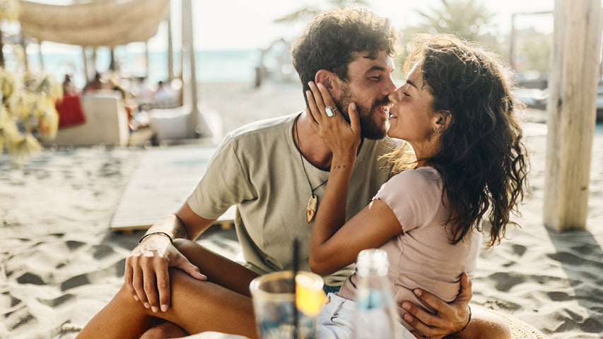 Couple leaning in to kiss each other on a beach near a cabana.