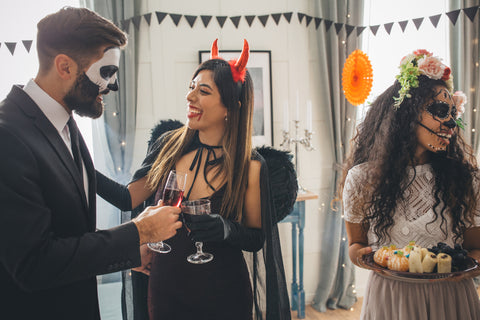 People interact at a party while wearing costumes like masks and devil horns.