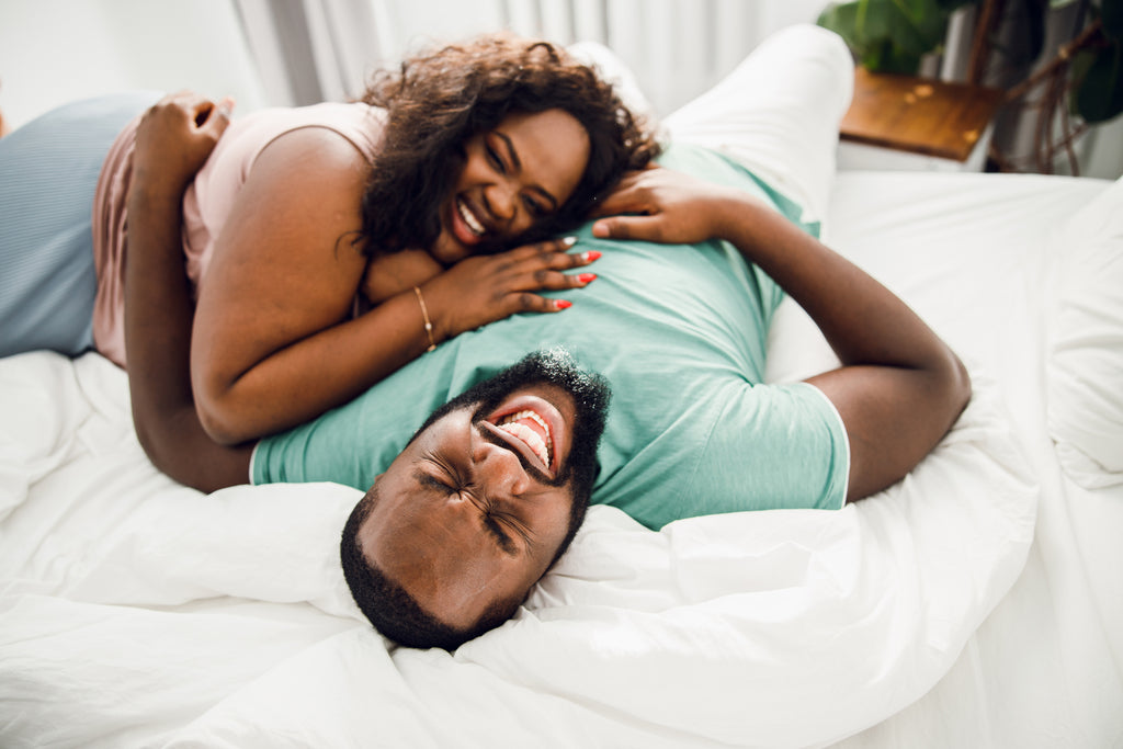 Partners laughing together while holding each other playfully in bed.