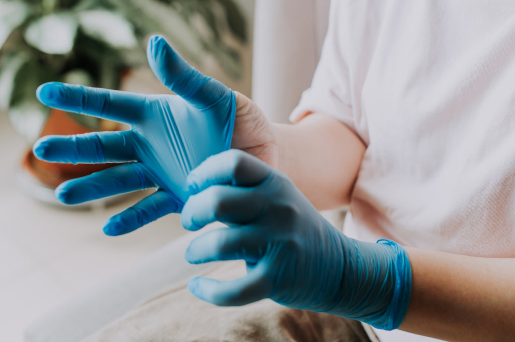 A person puts on a pair of blue latex gloves.