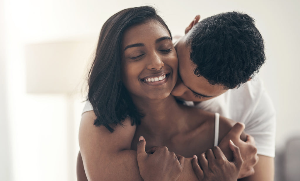 A man kisses his partner's neck while they embrace.