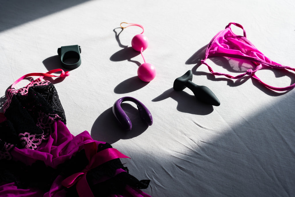 A variety of sex toys and lingerie on a white sheet.