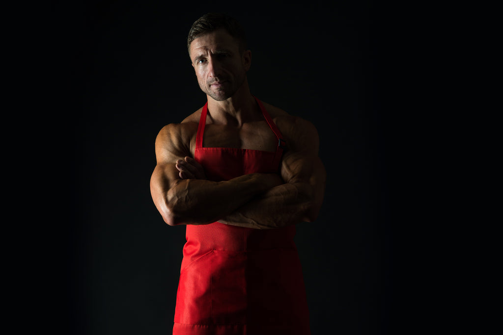 Man stands with arms folded in a red apron.