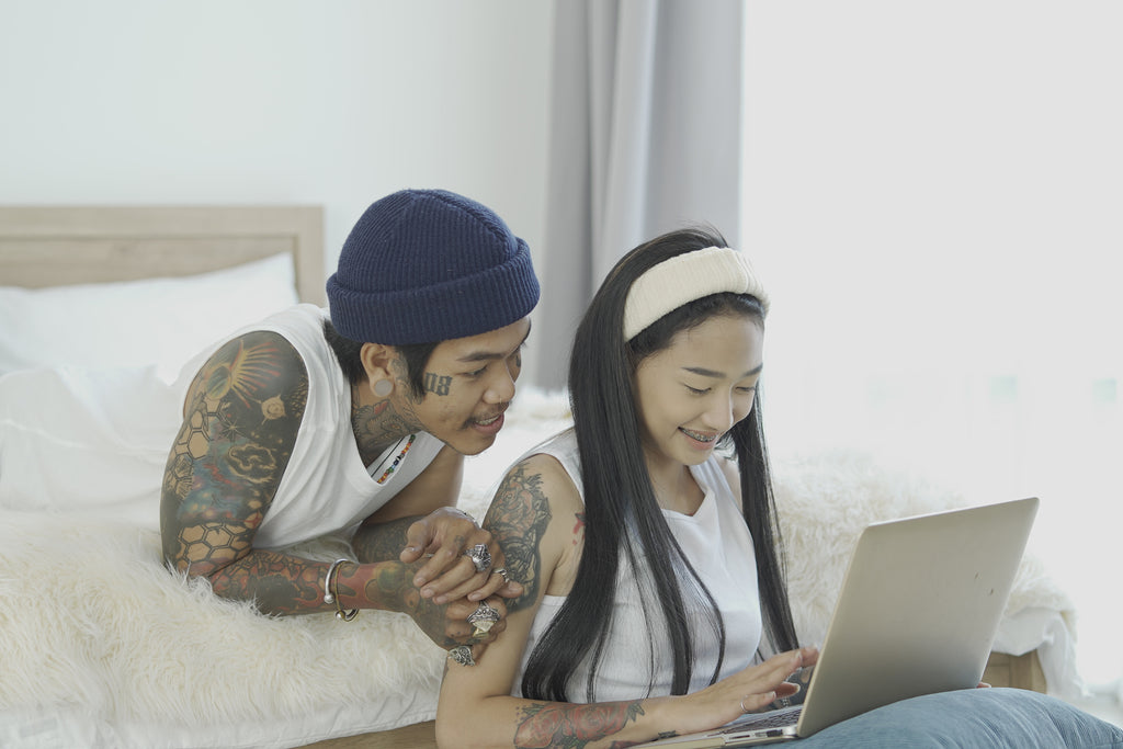 A couple looks at a laptop together in a bedroom.