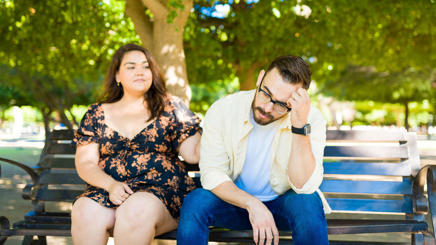 A woman’s hand touching the shoulder of her male partner as he’s staring into the distance.