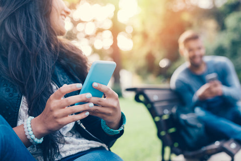 Un homme et une femme assis sur des bancs de parc qui se sourient et tiennent leurs téléphones.