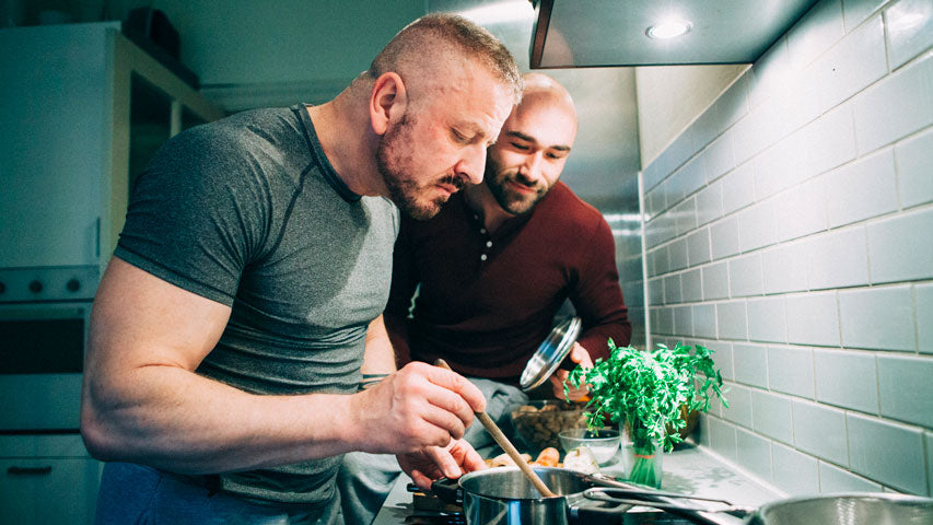 Deux hommes regardent leur casserole en cuisinant ensemble.