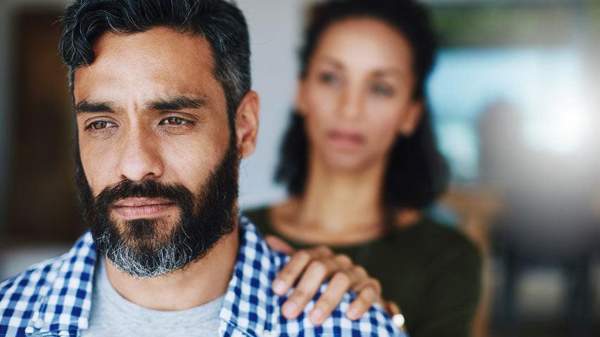 A woman’s hand touching the shoulder of her male partner as he’s staring into the distance.