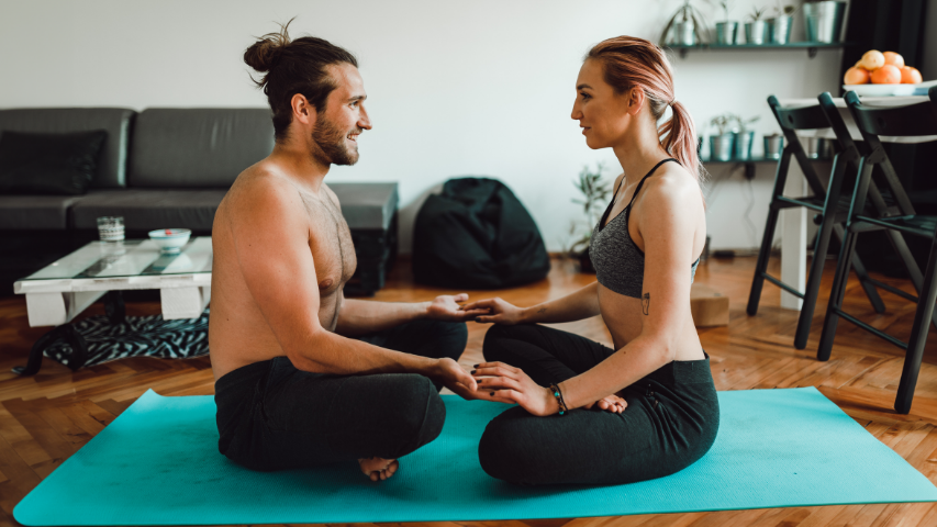 Two partners sitting cross-legged and facing each other while connecting with their fingertips touching preparing for erotic poses.