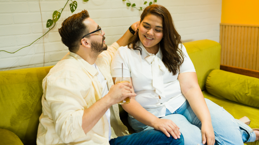 Un homme caresse les cheveux de sa partenaire qui lui rend son sourire, sur un sofa.