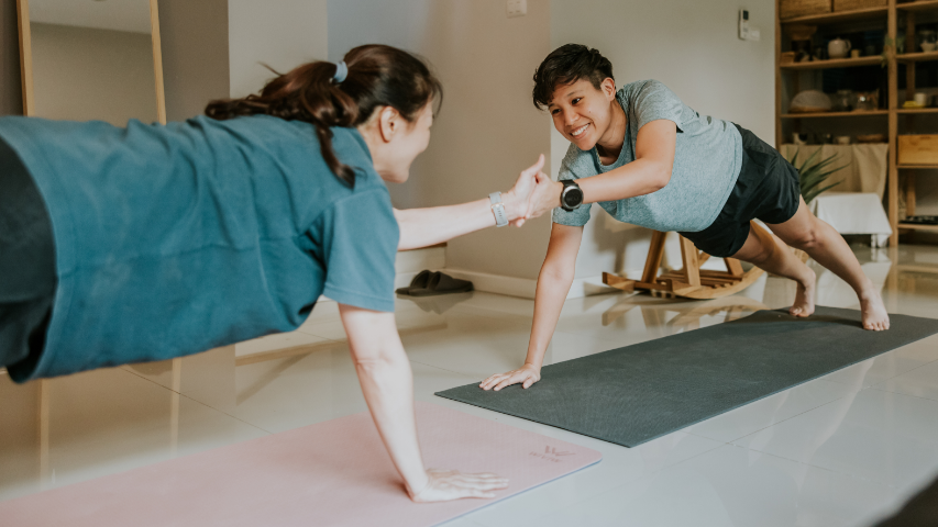 Two partners reaching their hands out to touch each other while getting into a yoga position.