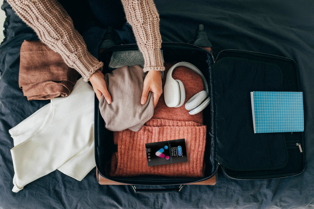 A person packs a suitcase with a package of Durex Mutual Climax condoms on top.