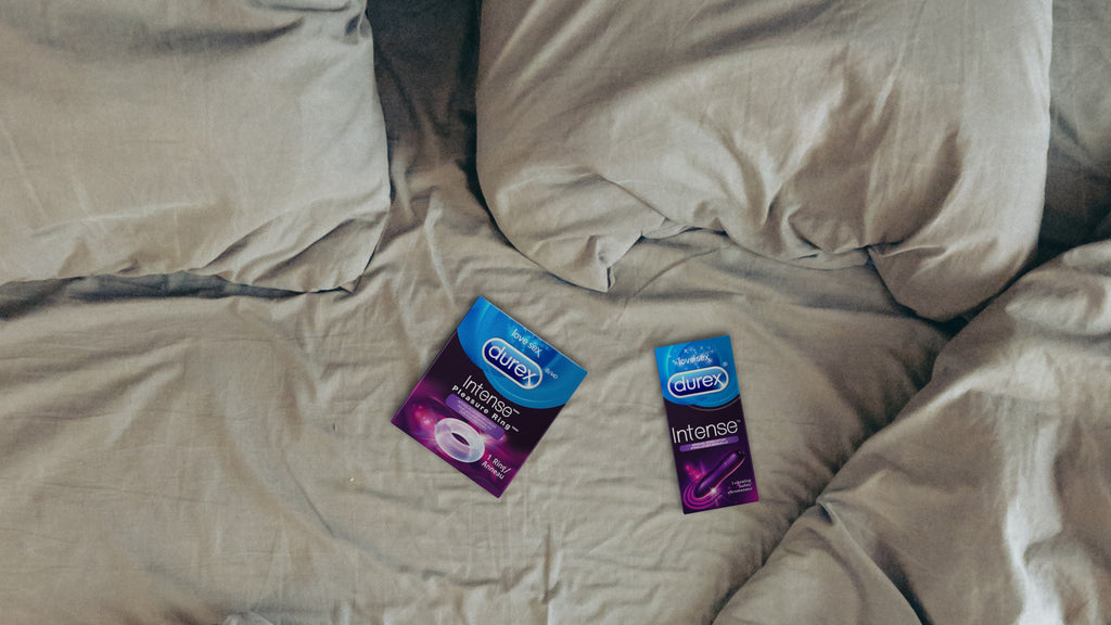 L’anneau pénien Durex Pleasure Ring et le vibromasseur Durex Intense dans leur emballage sur des draps beiges froissés.