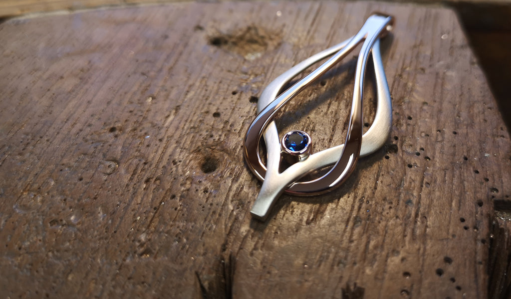Reef Knot pendant in 9ct rose and white gold, specially set with a sapphire 