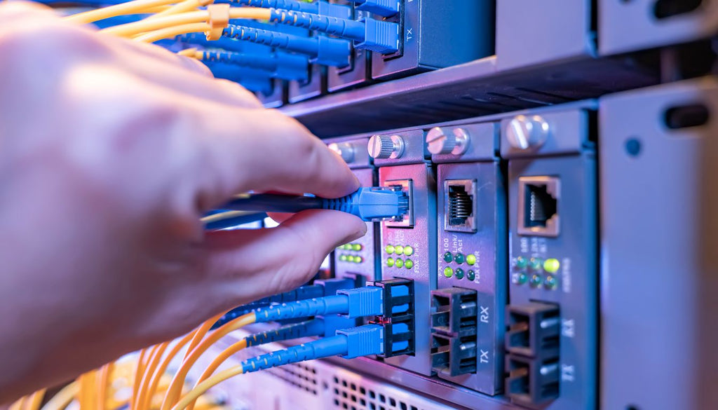 man working in network server room with Fiber Optic cables connected to optic ports and UTP