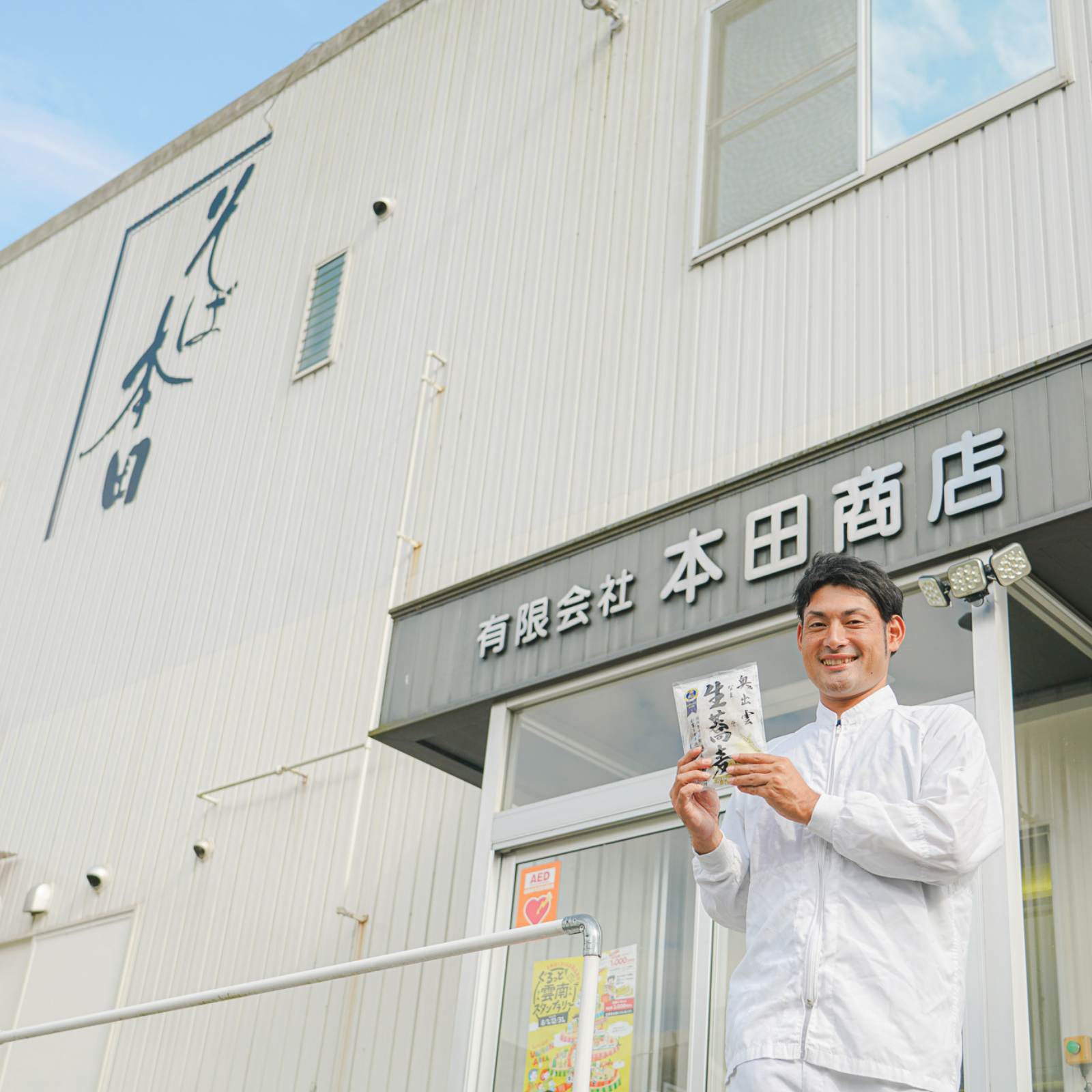 Craftsman holding a package of soba noodles in front of factory