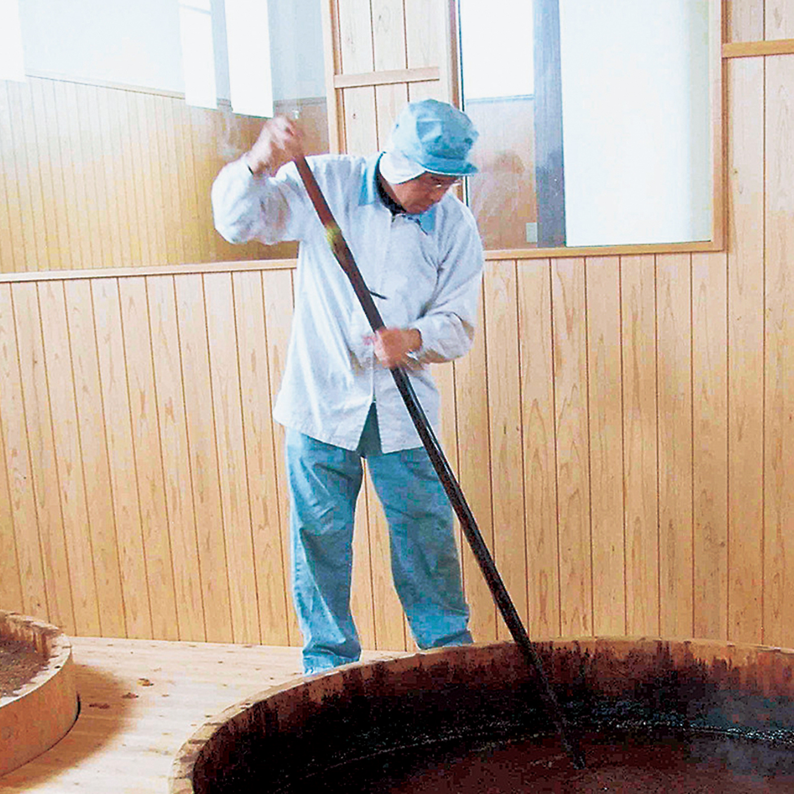 Craftsman stirring soy sauce in wooden barrel