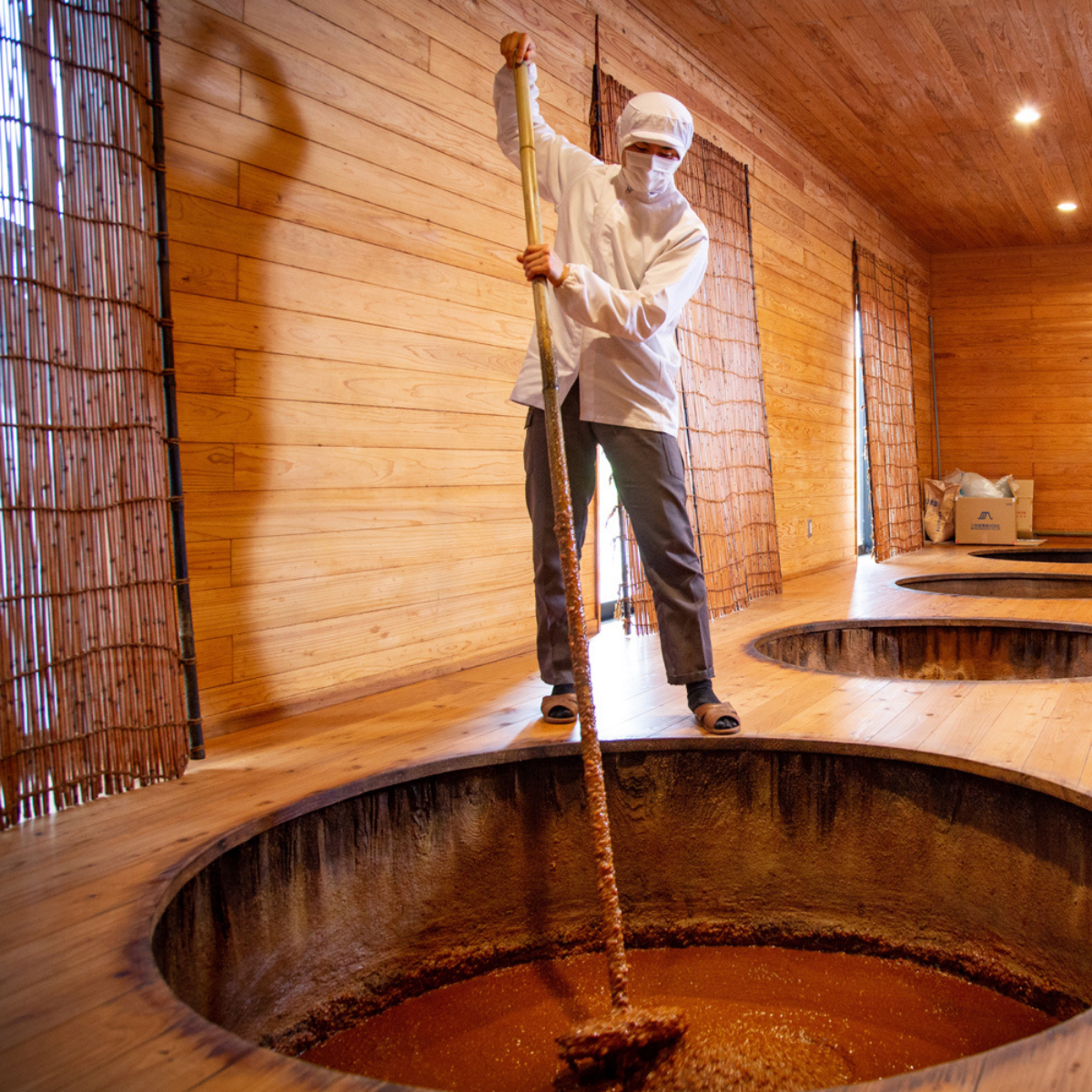 Man stirring soy sauce with a large wooden stick