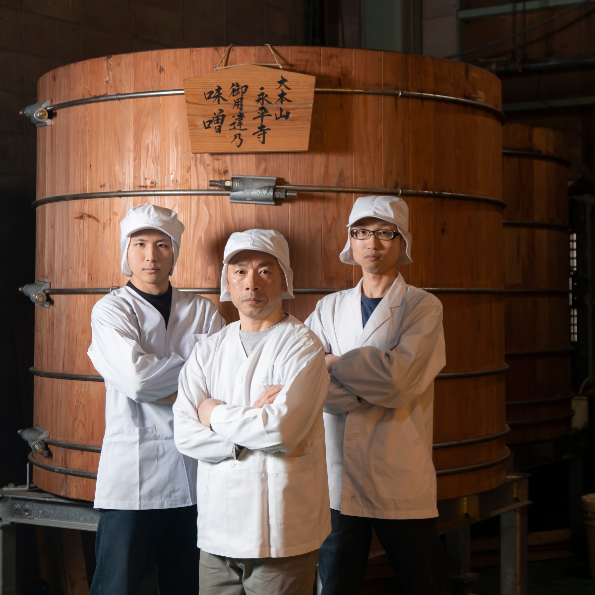 Three craftsmen standing in front of wooden miso barrel