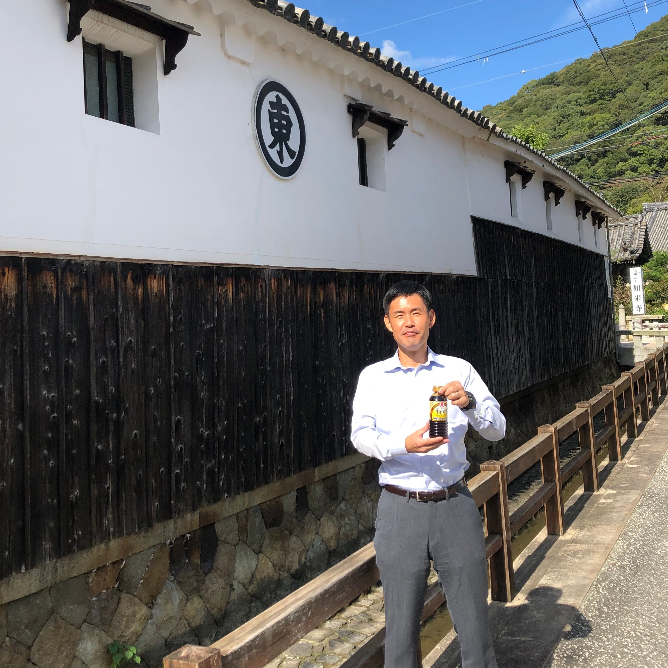 Man holding a bottle of soy sauce in front of factory