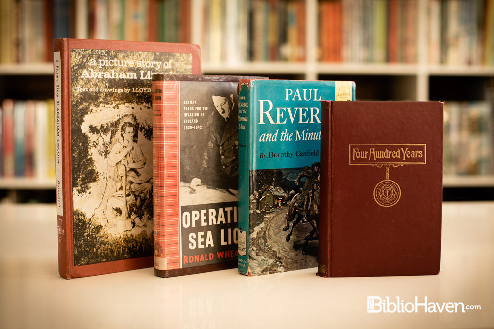 Four history and biography books shown in front of hundreds of books on a shelf blurred in the background.