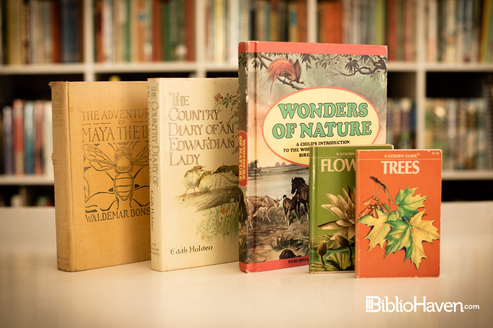 Five nature and animal books shown in front of hundreds of books on a shelf blurred in the background.