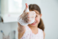 Child giving thumbs-up while washing hands