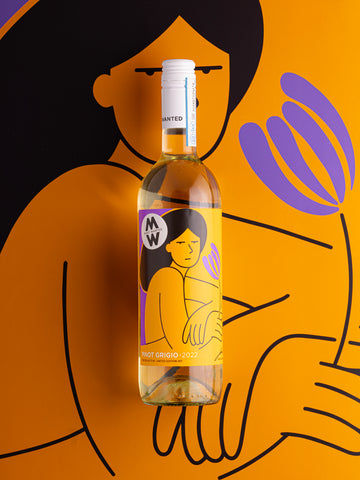 A white wine bottle of Pinot Grigio is seen laying on a large reproduction of its label. The label depicts a bold orange illustration of a serious woman looking straight at the viewer, while holding a purple flower in her hand, illustrated by Ana Curbelo.