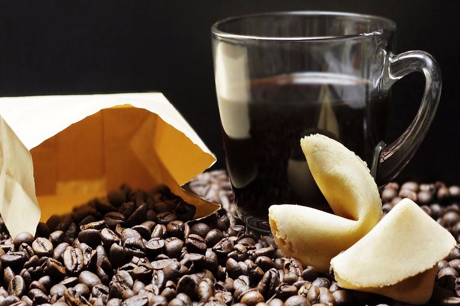 Paper bags, coffee cup and fortune cookie on top of a bed of coffee beans