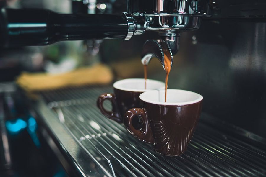 Coffee pouring out of an espresso machine into 2 brown cups