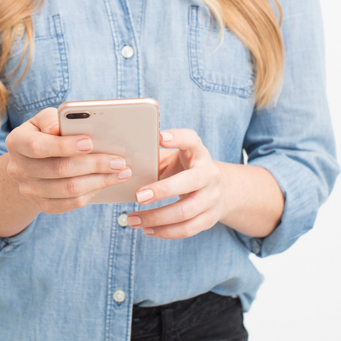 woman wearing blue shirt and black jeans holding a pink iphone