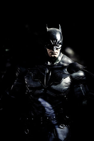 Man in a batman costume with a black background and a very serious look on his face