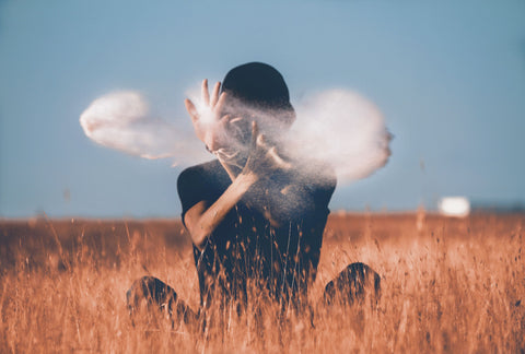 Guy sitting in a field moving smoke with his hands