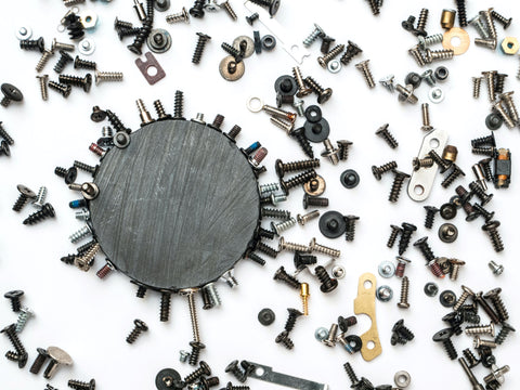 A magnet surrounded by screws on a white table, some of the screws are attached to the magnet