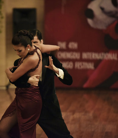 A couple dancing tango, they are mid turn with a dance studio behind them