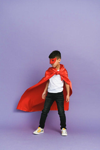 Boy in a red cape and superhero eye mask with a purple background