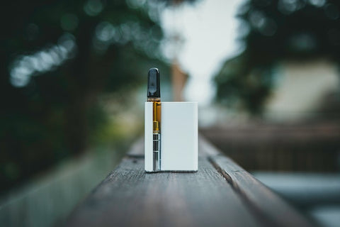 White Vape on wood with green trees and sky in the background