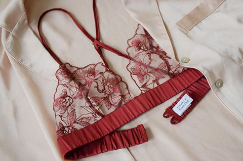Fleur of England red luxury lingerie embroidered boudoir bra placed on a silk blush pyjama shirt
