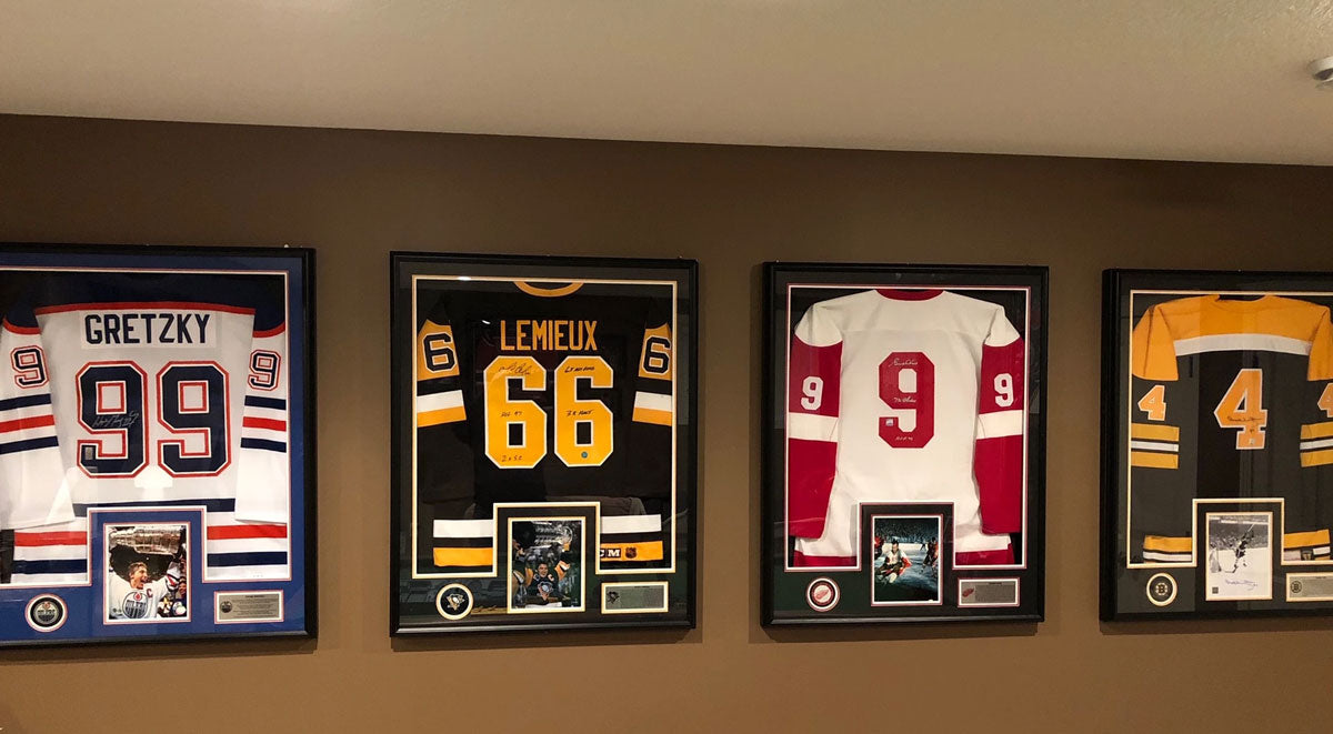 My man cave wall of framed jerseys with hats and signed pucks