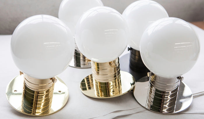 A group of polished brass and polished nickel mini globe flush mount light fixtures with a ribbed neck and small white round glass shade designed by Commune for Remains Lighting