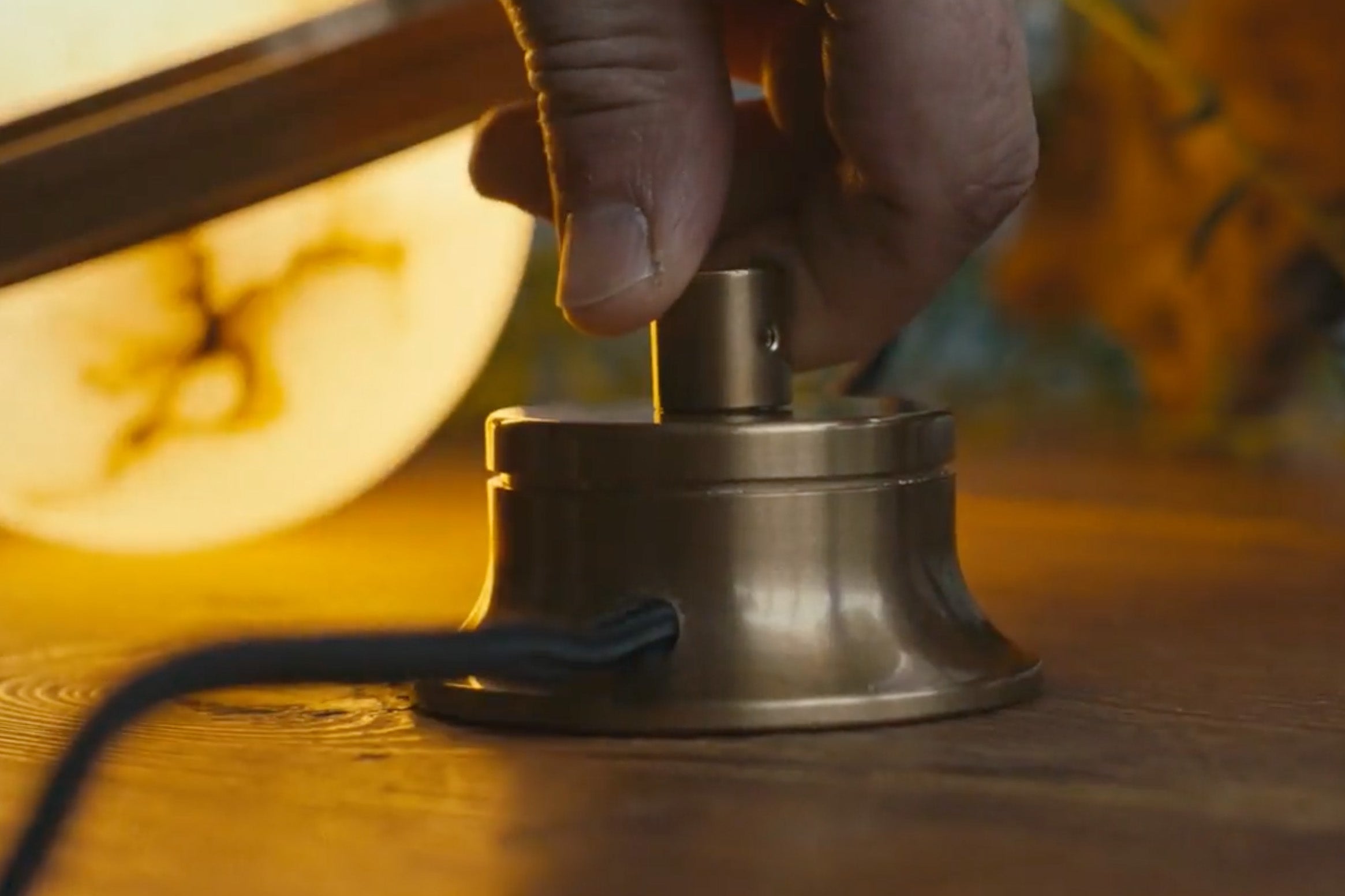 A custom antique brass rotary dimmer with integrated dim to warm LED lamping on a wooden table is switched on by hand, with a lit alabaster globe in the background.