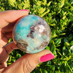Amazonite sphere with Lepidolite held in front of a bush