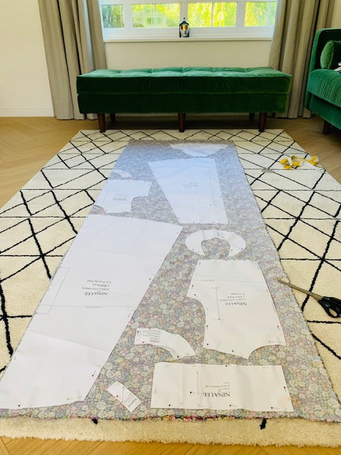 Fabric laid out on the floor with sewing pattern pieces attached ready to cut out