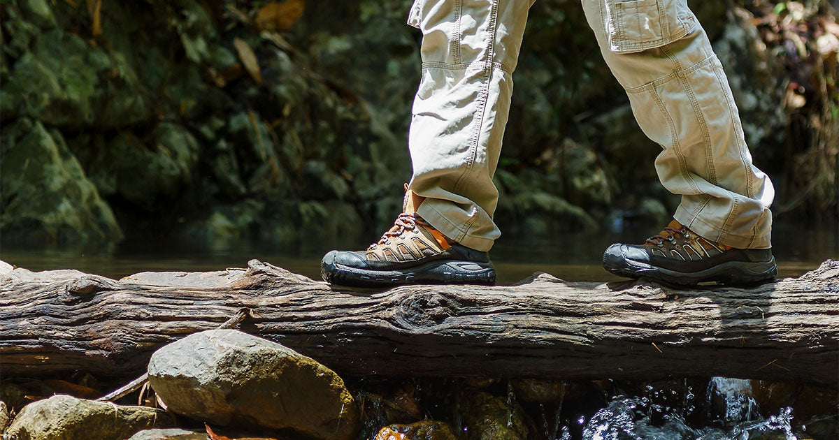 Man wearing hiking boots walking across log